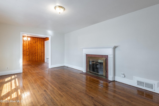 unfurnished living room with a brick fireplace, baseboards, visible vents, and hardwood / wood-style floors