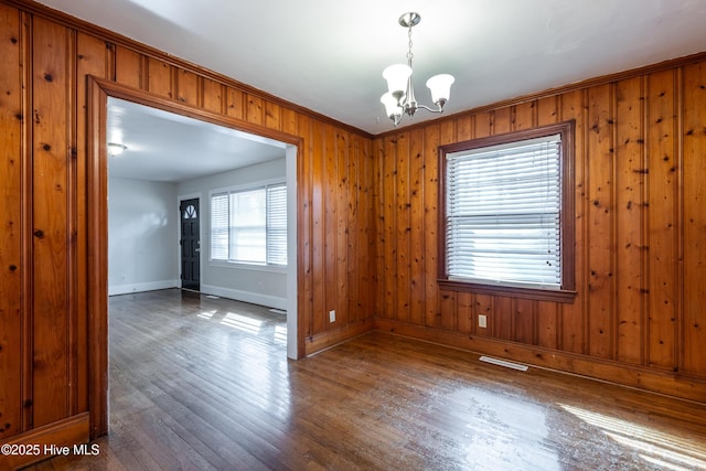 unfurnished room with visible vents, a notable chandelier, baseboards, and wood finished floors