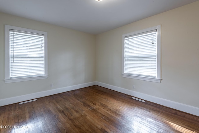 unfurnished room with hardwood / wood-style floors, visible vents, and baseboards