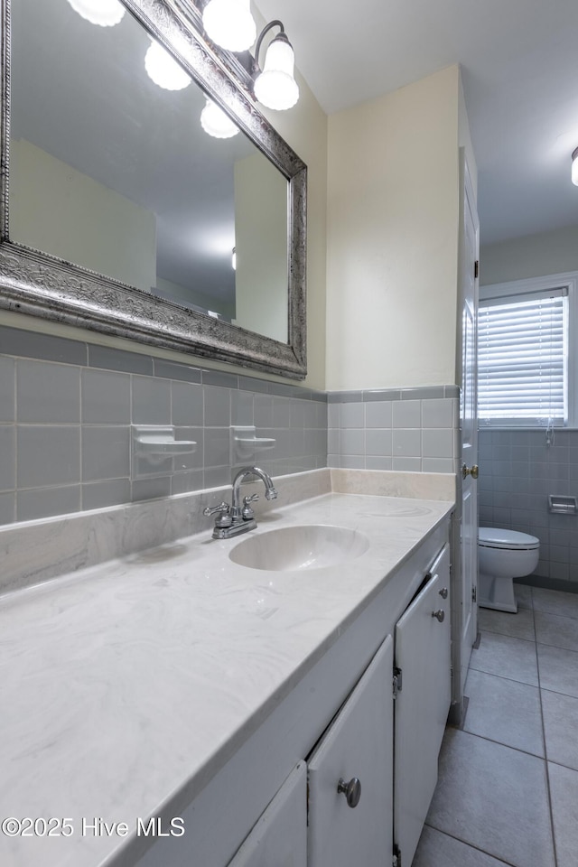 bathroom featuring toilet, a wainscoted wall, tile patterned floors, vanity, and tile walls