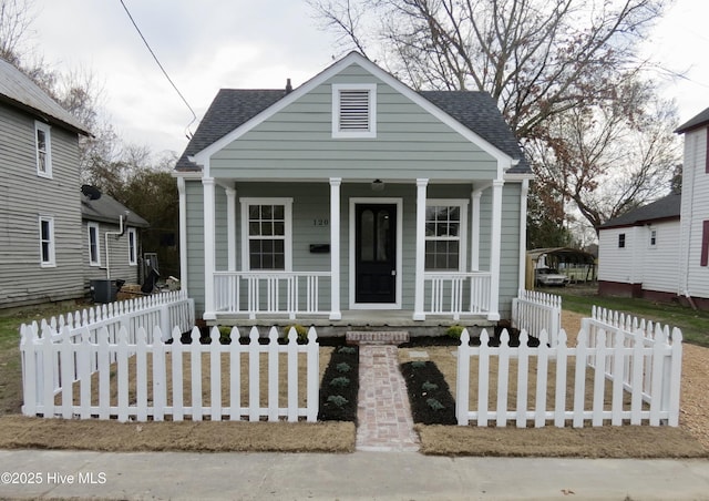 bungalow with covered porch, a fenced front yard, and roof with shingles