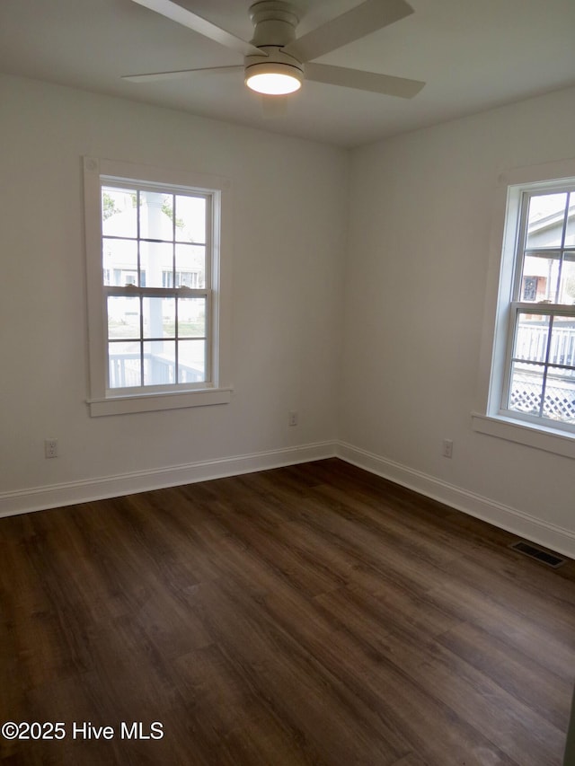 empty room with dark wood finished floors, visible vents, and baseboards