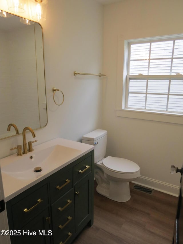 bathroom with toilet, wood finished floors, vanity, visible vents, and baseboards