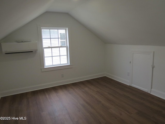 additional living space with lofted ceiling, dark wood-type flooring, a wall unit AC, and baseboards