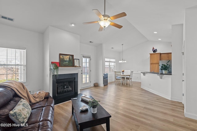 living room with visible vents, a fireplace with flush hearth, lofted ceiling, ceiling fan with notable chandelier, and light wood-style floors