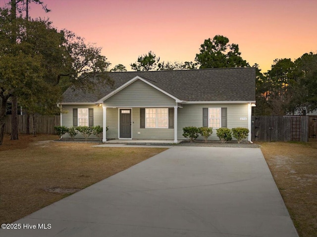 single story home with covered porch, roof with shingles, a front yard, and fence