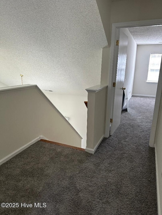 corridor featuring a textured ceiling, carpet floors, an upstairs landing, and baseboards