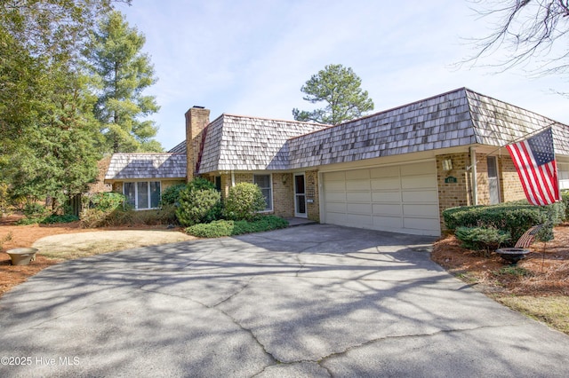 view of front of property with mansard roof, an attached garage, brick siding, driveway, and a chimney