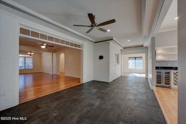 unfurnished living room with arched walkways, ornamental molding, dark wood-type flooring, and baseboards