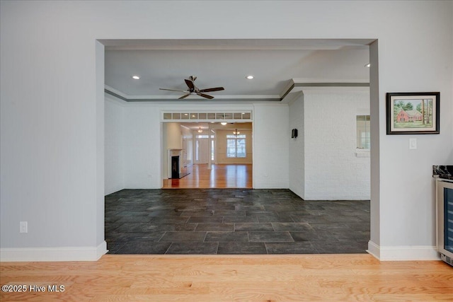 interior space with ornamental molding, a fireplace, ceiling fan, and wood finished floors