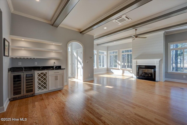 bar featuring indoor wet bar, a fireplace with flush hearth, light wood-style floors, beverage cooler, and beamed ceiling