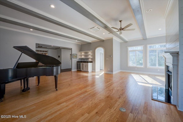 living area with ceiling fan, a fireplace, arched walkways, baseboards, and beamed ceiling