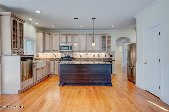 kitchen with appliances with stainless steel finishes, arched walkways, a center island, ornamental molding, and glass insert cabinets
