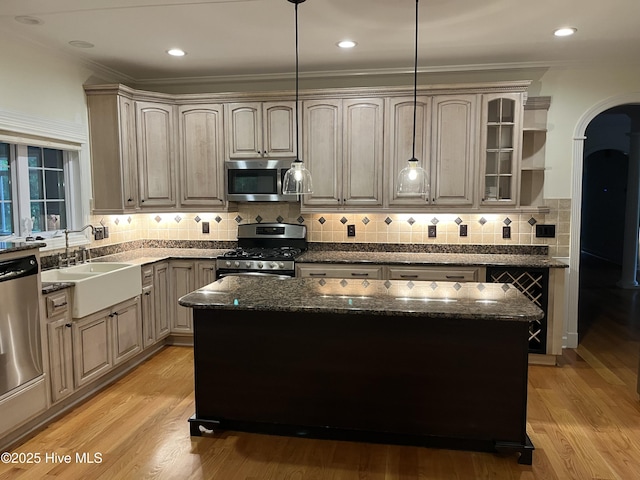 kitchen with a sink, arched walkways, dark stone counters, stainless steel appliances, and ornamental molding