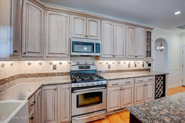 kitchen with glass insert cabinets, light wood-type flooring, a chandelier, tasteful backsplash, and stainless steel appliances