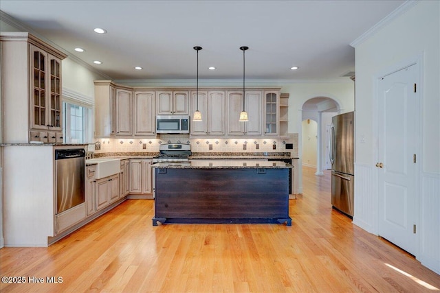 kitchen with glass insert cabinets, appliances with stainless steel finishes, arched walkways, and a center island