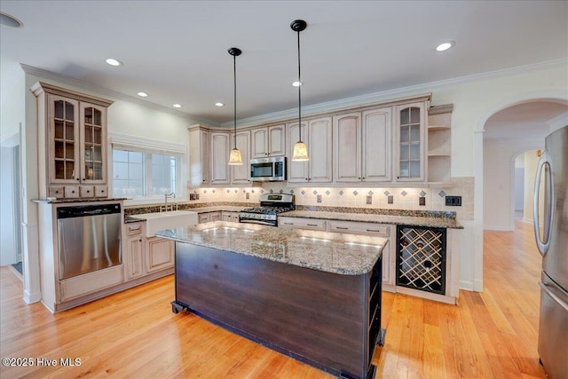 kitchen featuring light wood finished floors, tasteful backsplash, arched walkways, stainless steel appliances, and a sink