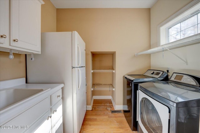 clothes washing area featuring light wood-style floors, baseboards, washing machine and clothes dryer, a sink, and cabinet space