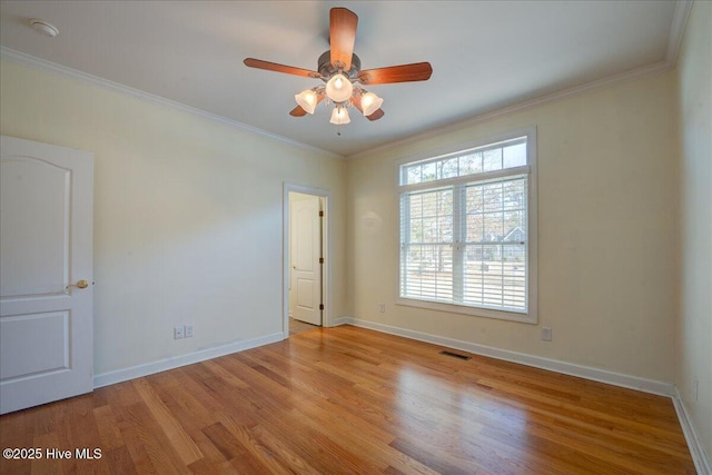 empty room featuring ceiling fan, visible vents, wood finished floors, baseboards, and ornamental molding