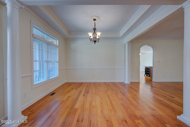 empty room with arched walkways, crown molding, decorative columns, a raised ceiling, and light wood-type flooring