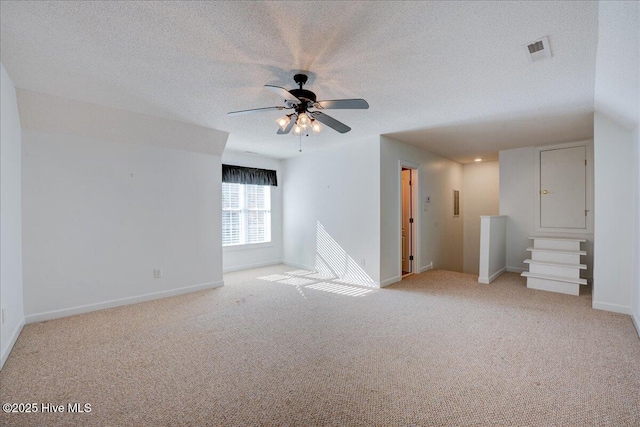 empty room featuring light colored carpet, ceiling fan, a textured ceiling, and baseboards