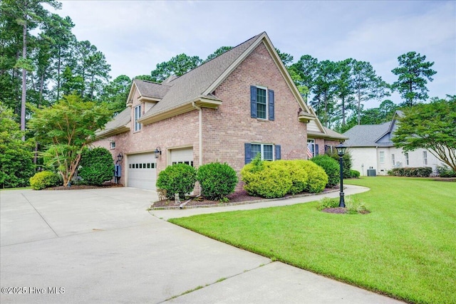 view of side of home with brick siding, a shingled roof, a yard, and concrete driveway