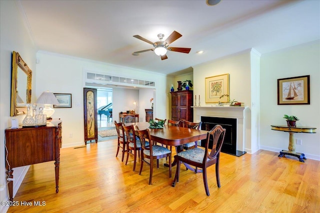 dining room featuring light wood-style floors, ornamental molding, and a fireplace with raised hearth