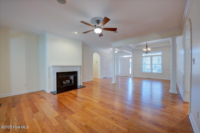 unfurnished living room featuring a fireplace with raised hearth, ornamental molding, light wood-type flooring, ornate columns, and ceiling fan with notable chandelier