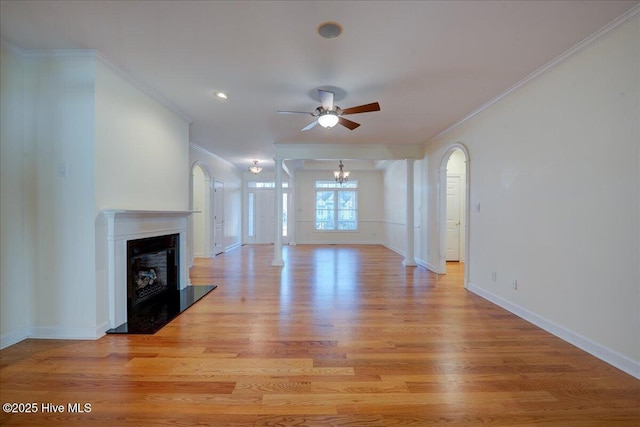 unfurnished living room featuring a fireplace with raised hearth, ornamental molding, light wood-type flooring, baseboards, and ceiling fan with notable chandelier