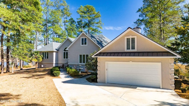 view of front of home featuring a detached garage, a chimney, metal roof, a standing seam roof, and stucco siding