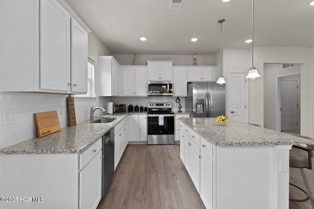 kitchen featuring visible vents, appliances with stainless steel finishes, a kitchen island, a sink, and wood finished floors