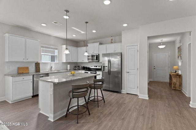 kitchen featuring stainless steel appliances, light wood-type flooring, a kitchen island, and white cabinetry