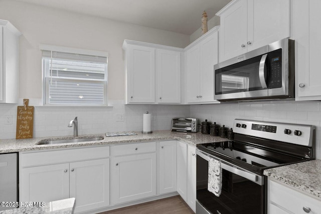 kitchen featuring appliances with stainless steel finishes, a sink, light stone countertops, white cabinetry, and backsplash