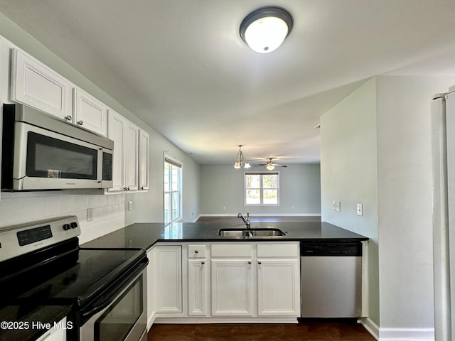 kitchen with stainless steel appliances, a peninsula, a sink, white cabinetry, and dark countertops