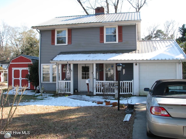 traditional home with metal roof, a porch, an attached garage, a storage unit, and a chimney