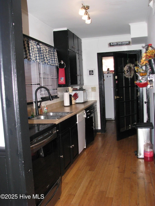 kitchen with white appliances, light wood-style flooring, dark cabinets, and a sink