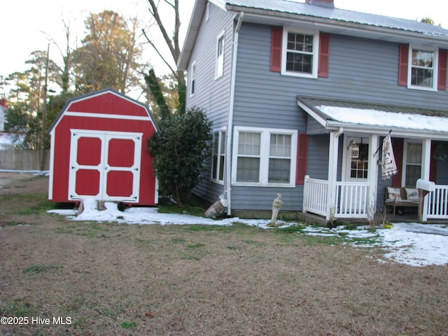 view of front of home featuring metal roof, covered porch, an outdoor structure, a shed, and a front yard