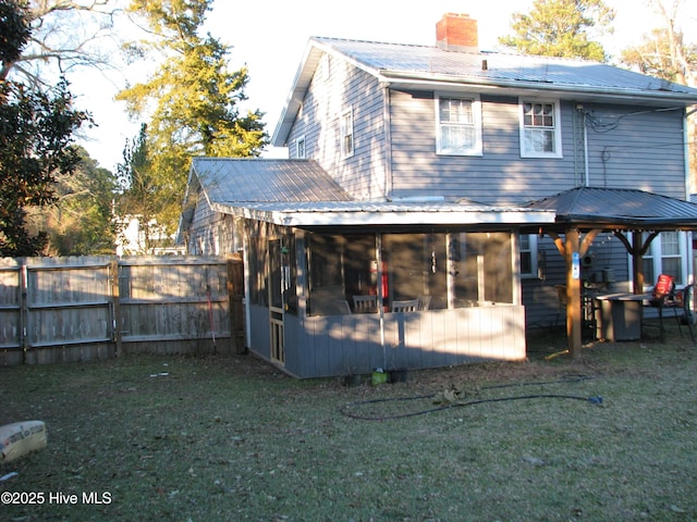 back of property with a chimney, a lawn, a sunroom, metal roof, and fence