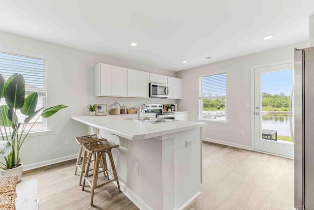 kitchen featuring a breakfast bar, stainless steel appliances, light countertops, light wood-style flooring, and white cabinets