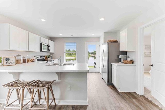 kitchen featuring light countertops, appliances with stainless steel finishes, a sink, a peninsula, and a kitchen breakfast bar