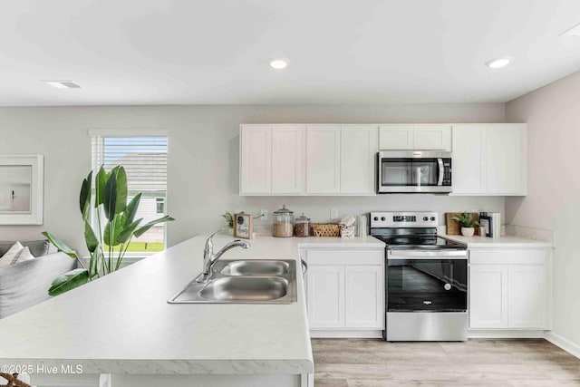 kitchen featuring stainless steel appliances, a peninsula, a sink, white cabinetry, and light countertops