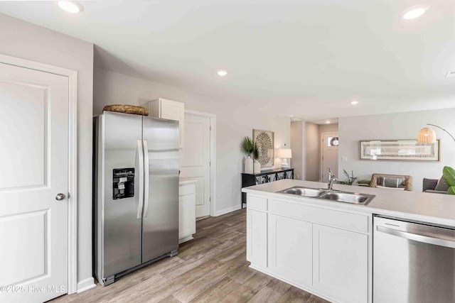 kitchen with a sink, white cabinetry, light countertops, appliances with stainless steel finishes, and light wood-type flooring