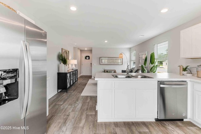 kitchen with light wood-style flooring, a peninsula, a sink, white cabinetry, and appliances with stainless steel finishes