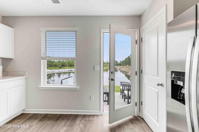 doorway to outside featuring baseboards, a water view, and light wood finished floors