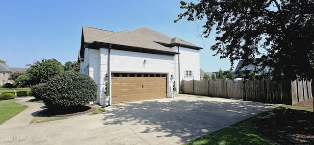 view of property exterior featuring brick siding, driveway, an attached garage, and fence