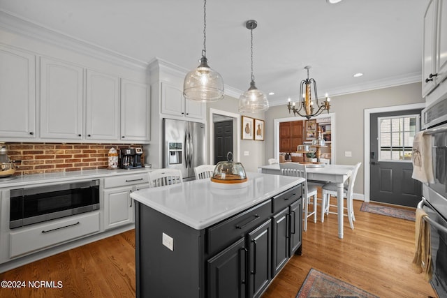 kitchen with stainless steel appliances, white cabinets, crown molding, and wood finished floors