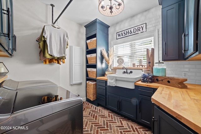 kitchen featuring tasteful backsplash, wood counters, blue cabinets, brick floor, and a sink