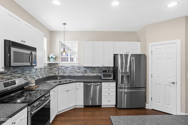 kitchen with dark countertops, appliances with stainless steel finishes, white cabinets, and a sink