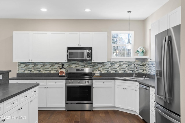 kitchen featuring dark countertops, appliances with stainless steel finishes, dark wood-type flooring, white cabinets, and a sink