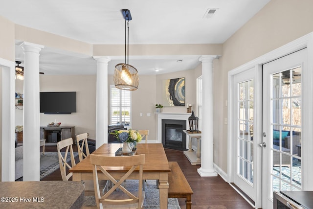 dining room featuring a glass covered fireplace, dark wood finished floors, visible vents, and ornate columns